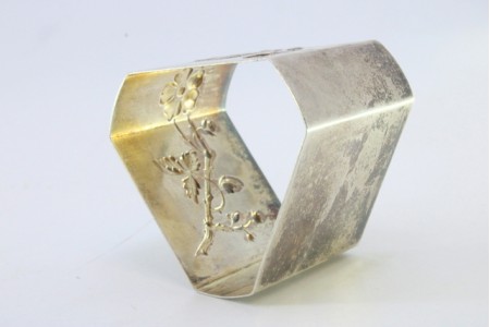 Argola de guardanapo em prata em forma triangular com flores relevadas.